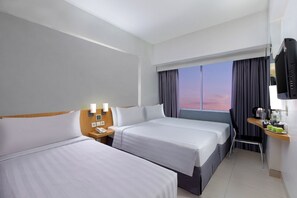 A hotel room with two beds, a desk with a chair, a TV, and a window with curtains. - favehotel Manahan - Solo (Surakarta)