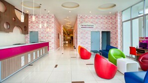 Un espace d’accueil d’hôtel au design moderne, comprenant un comptoir d’accueil, des sièges aux couleurs vives et un panneau indiquant le nom de l’hôtel.