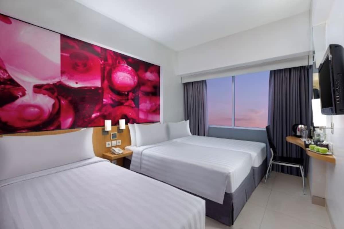 A hotel room with two beds, a large window with curtains, a desk with a chair, and a television.