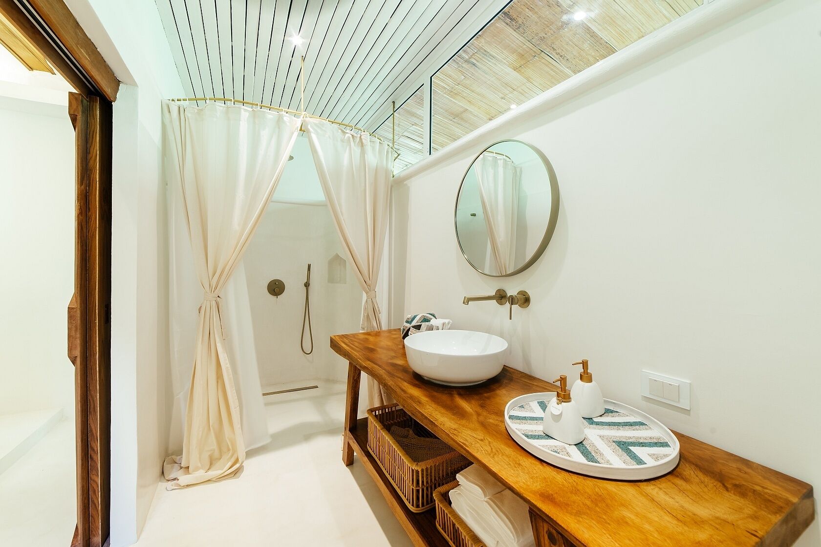 A modern bathroom with a wooden vanity, a round mirror, and a glass shower enclosure.