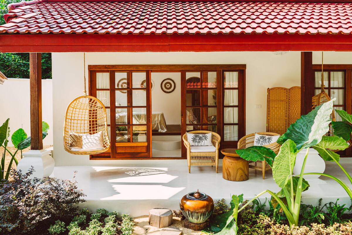 A traditional house with a tiled roof, a porch with wicker furniture, and a garden with tropical plants.