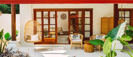 A traditional house with a tiled roof, a porch with wicker furniture, and a garden with tropical plants.