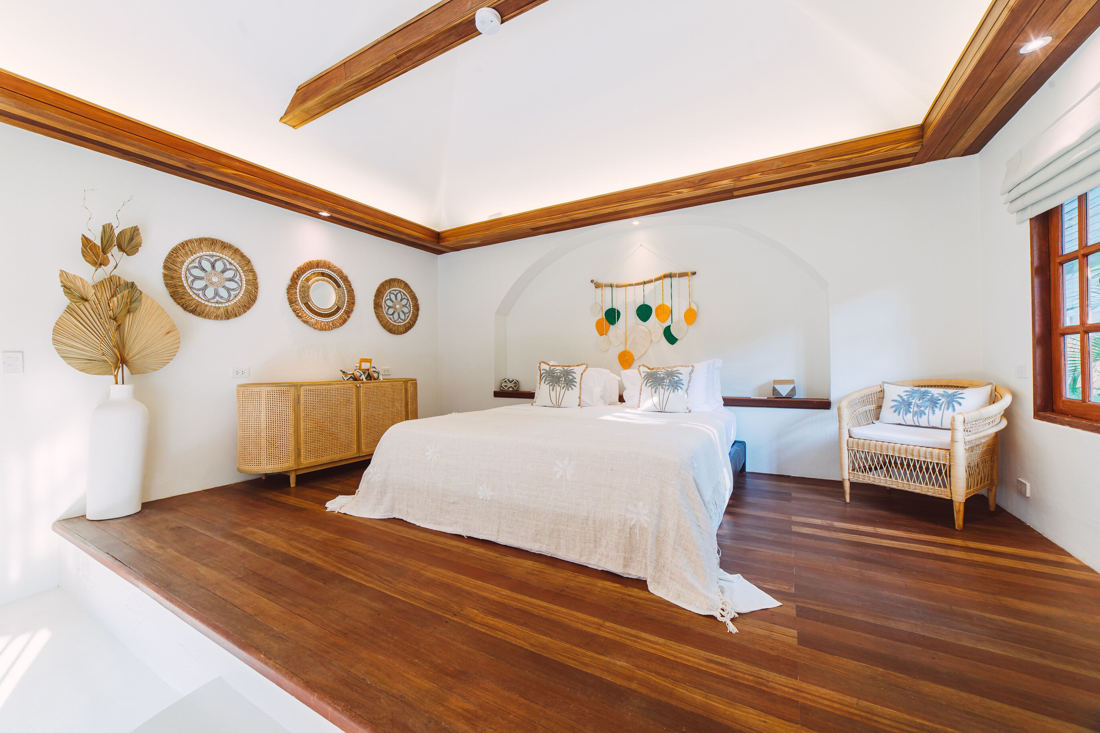 Ein geräumiges Schlafzimmer mit einem großen Bett, Holzbalkendecke und einem Korbstuhl.