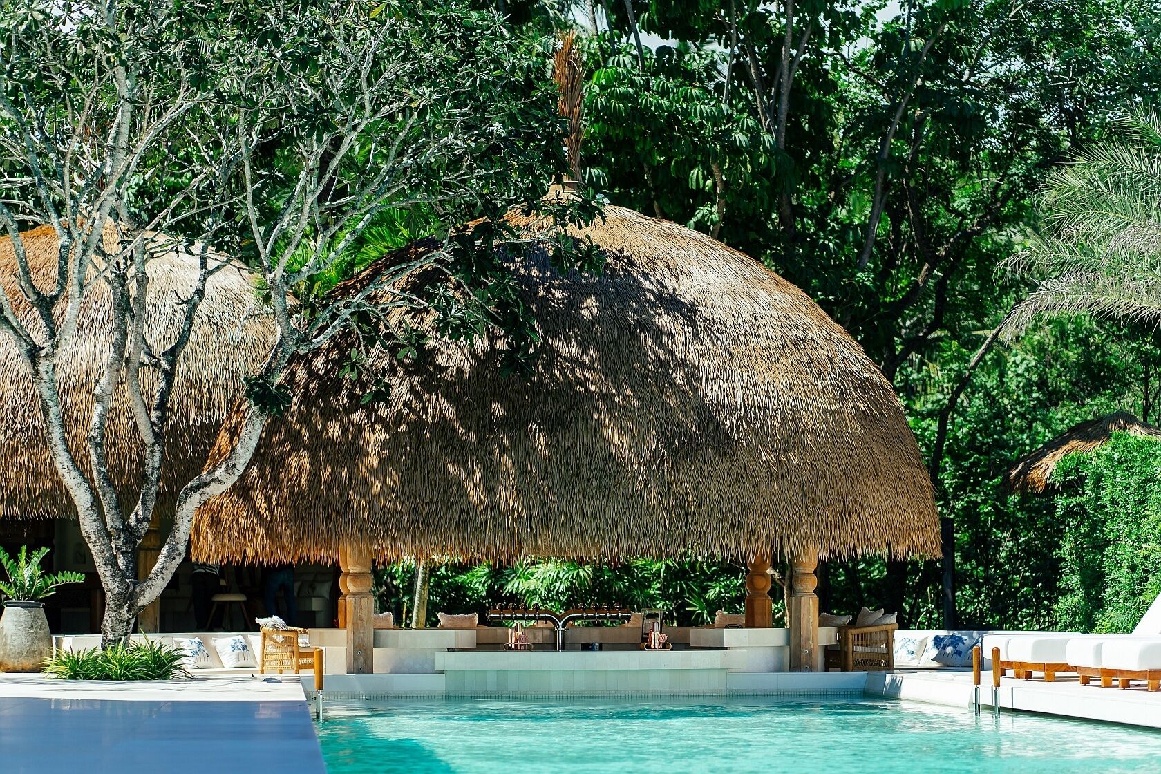 A pool area with thatched umbrellas and lounge chairs.