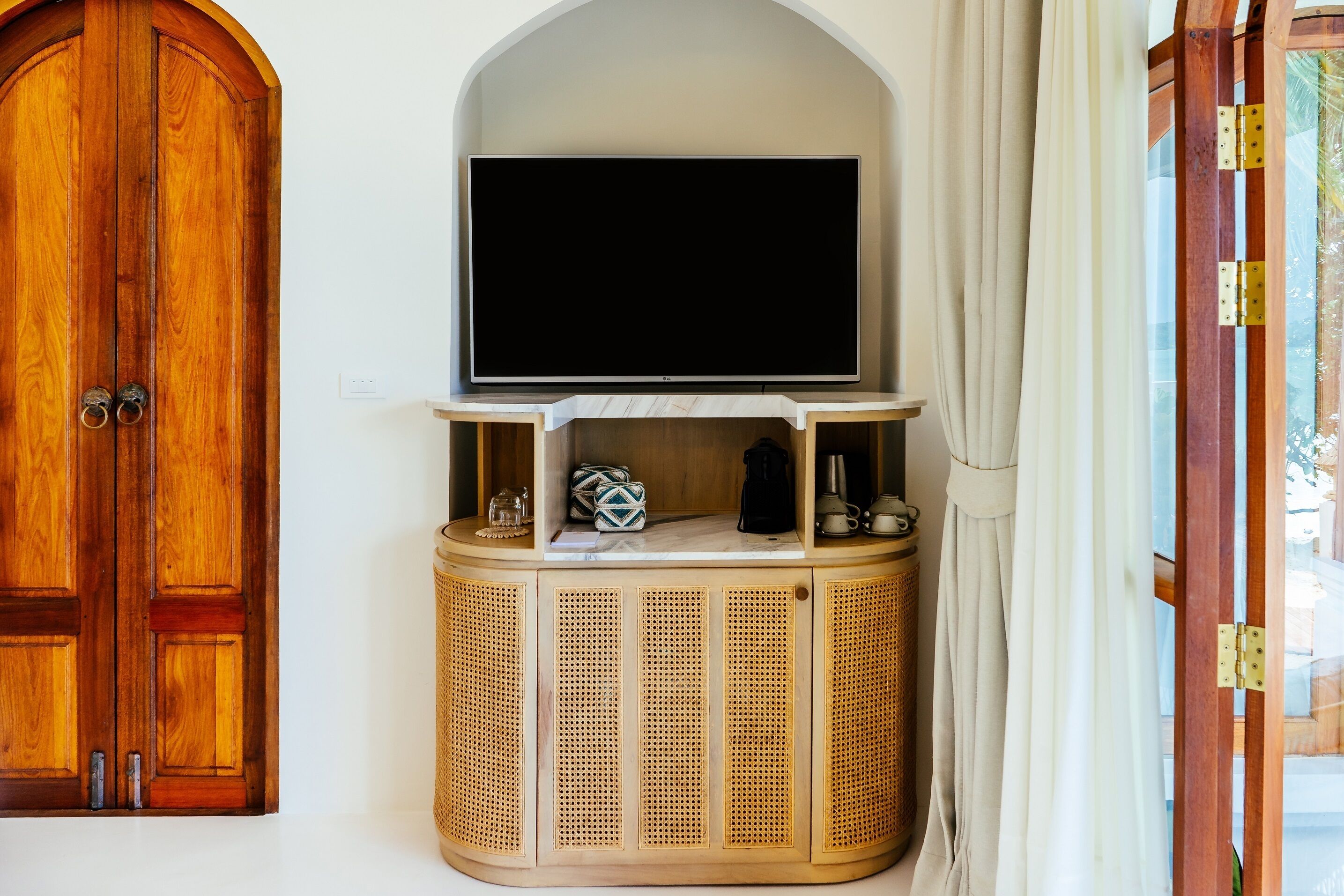 A wooden door, a flat-screen TV mounted on a wooden cabinet, and a glass door with a curtain.