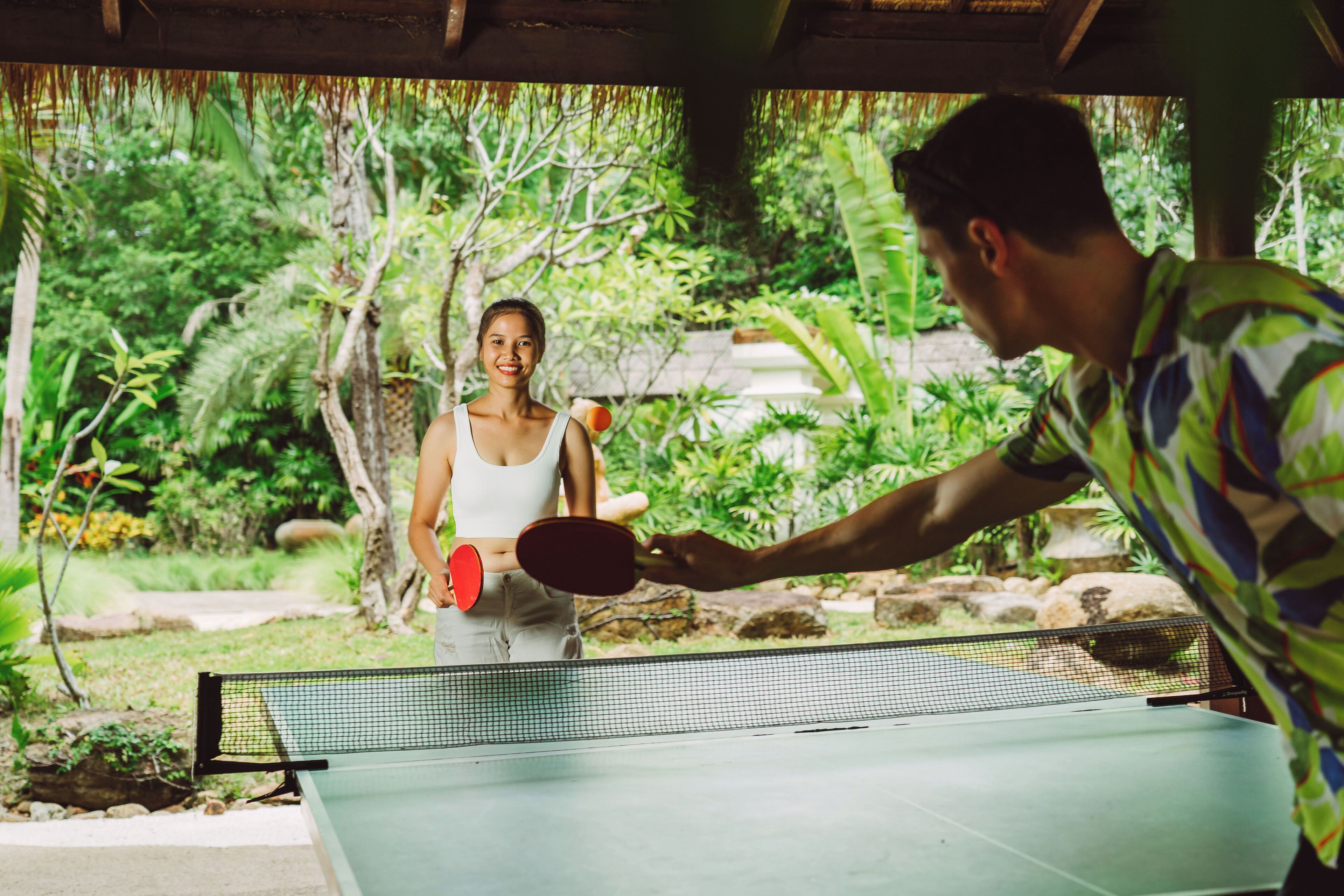 A table tennis table set up outdoors with a net in the middle, surrounded by lush greenery.