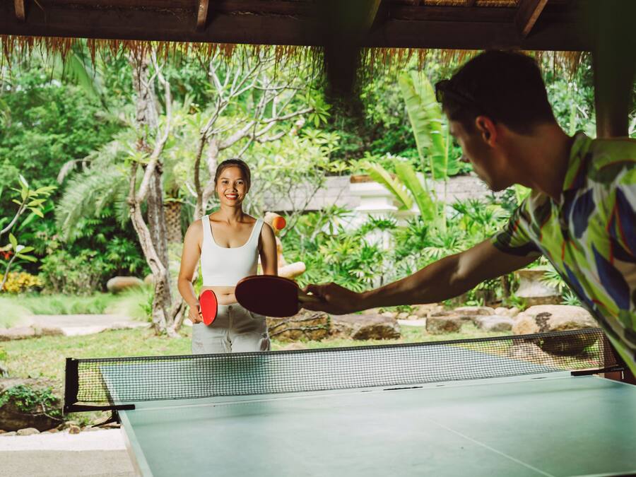 A table tennis table set up outdoors with a net in the middle, surrounded by lush greenery.