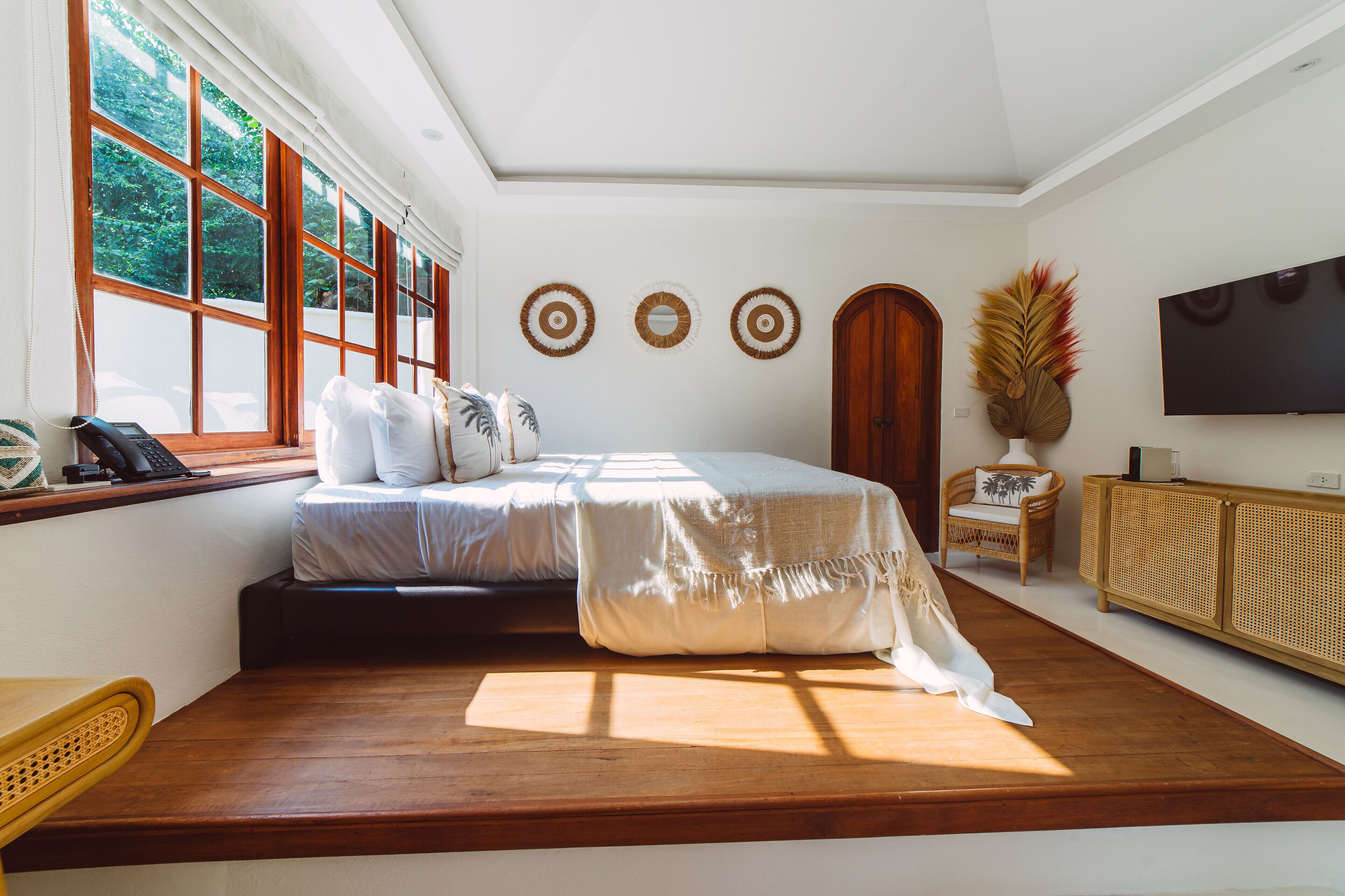 Ampia camera da letto con un letto grande, pavimento in legno, finestra con persiane, televisore e tavolino in rattan.