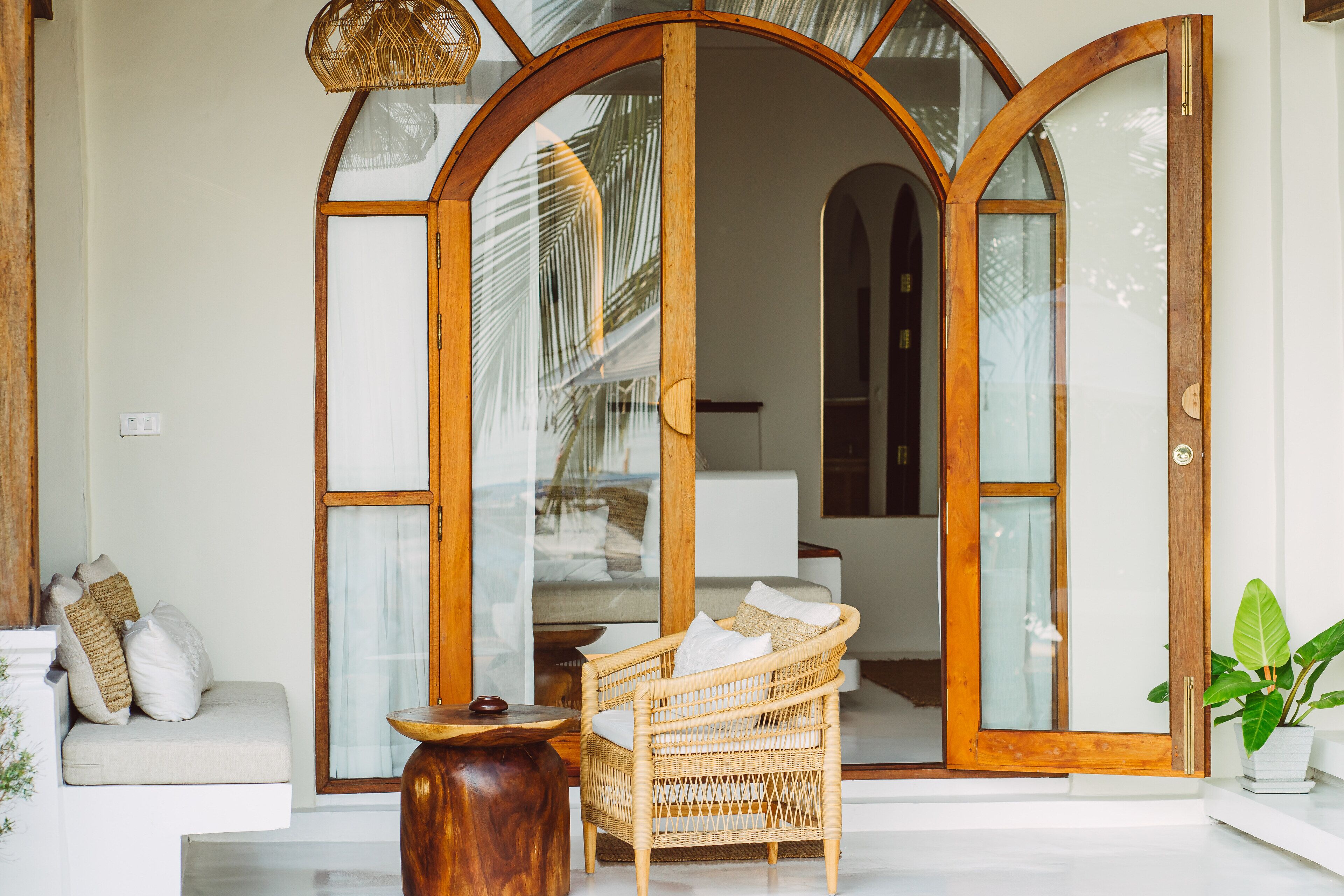 A room with a wicker chair, a wooden table, and a sofa with cushions.