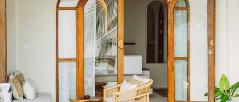 A room with a wicker chair, a wooden table, and a sofa with cushions.