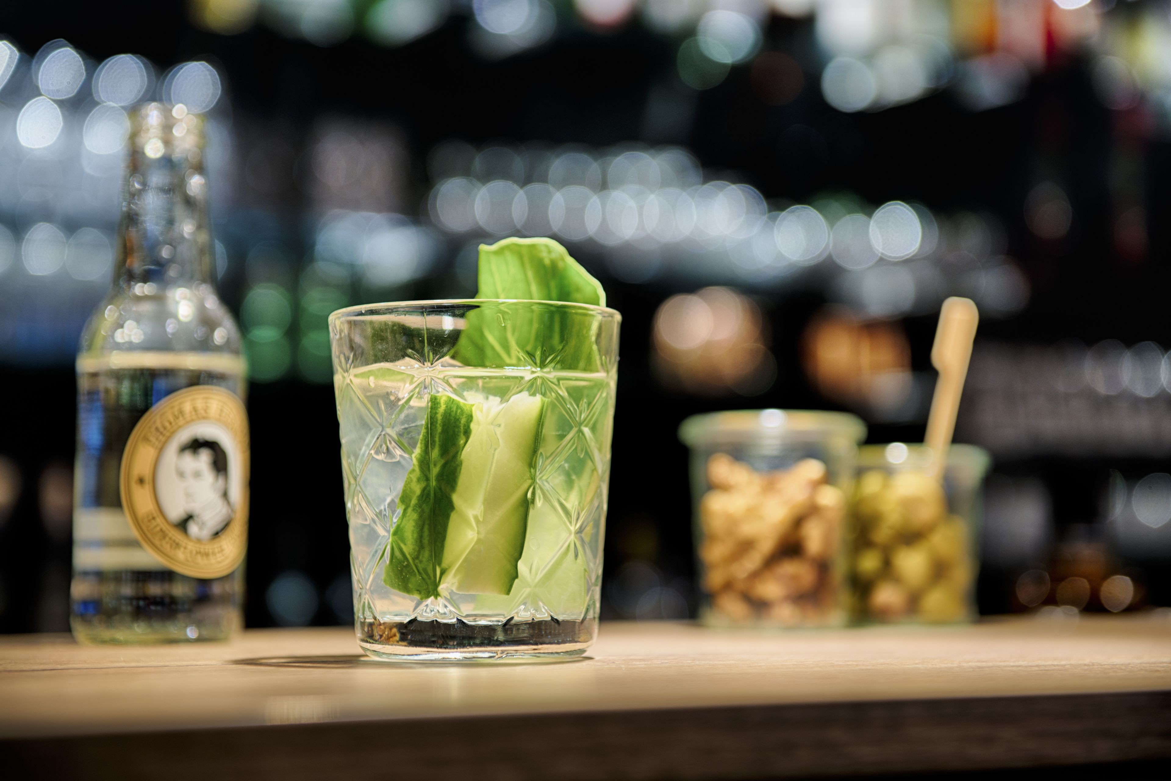 Un verre décoré d’une feuille de menthe sur le comptoir d’un bar, une bouteille avec une étiquette et un bocal rempli de noix.
