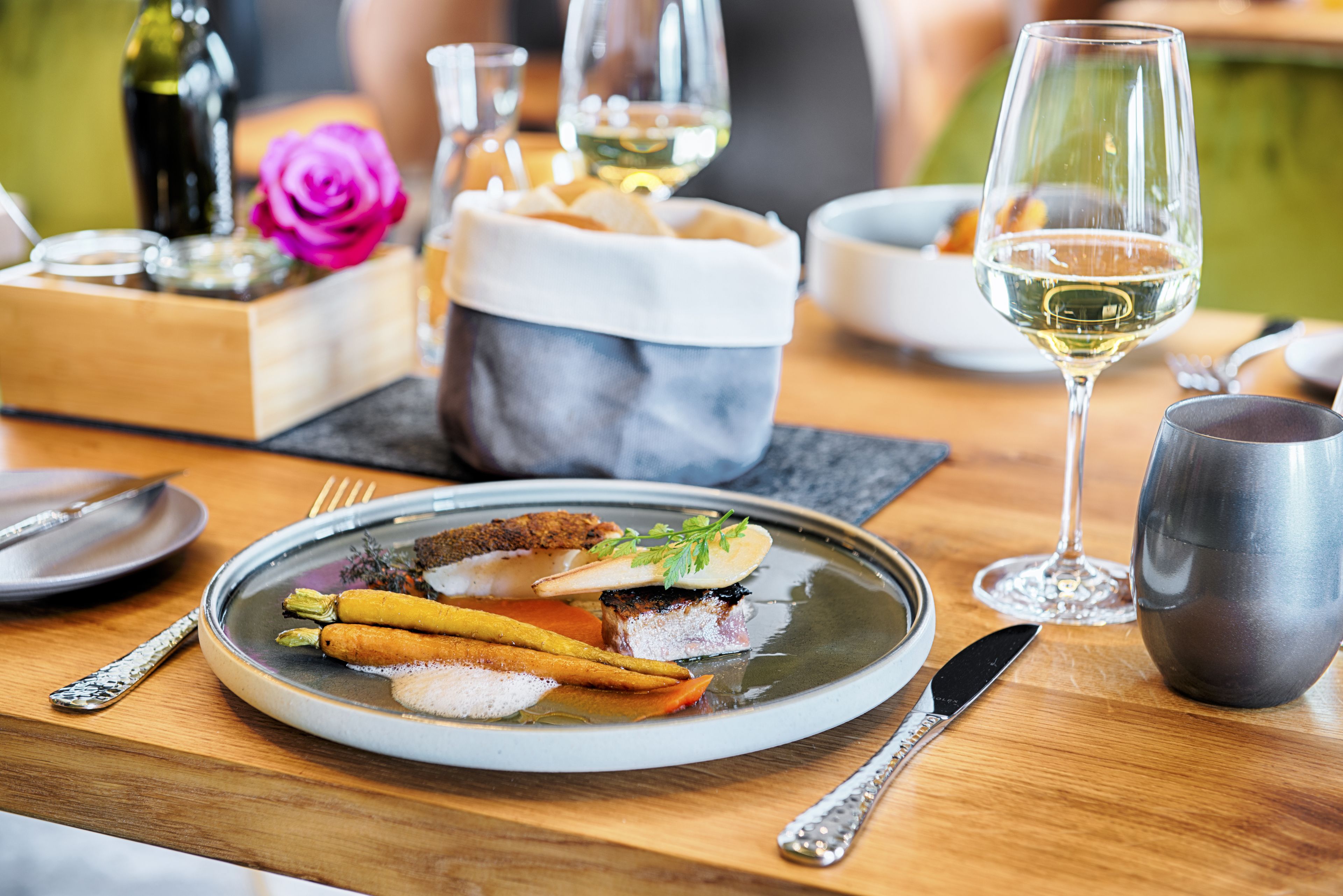 Una mesa de comedor con un plato de comida, una copa de vino y un vaso metálico.