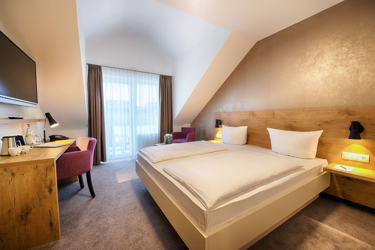 A hotel room with a large bed, a desk with a chair, a television, and a window with curtains.