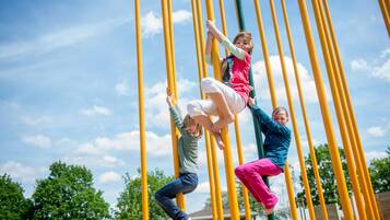 Niños trepando una serie de postes amarillos en un parque infantil.