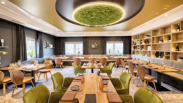 A spacious dining area with multiple tables and chairs, a central chandelier, and a wine display.