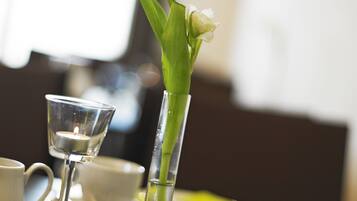 A dining table with a candle in a glass holder, a white flower in a clear vase, and a white cup and saucer.