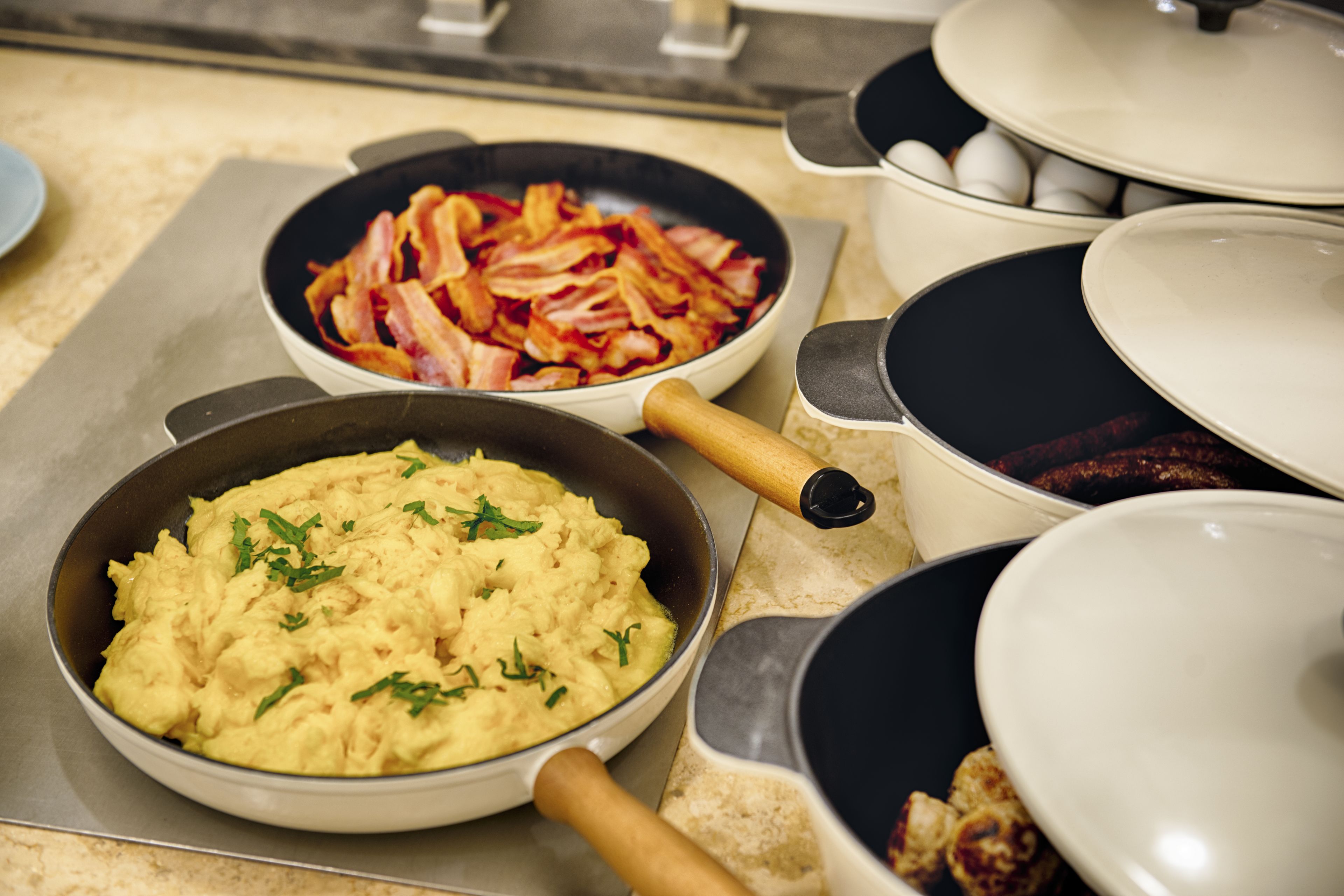 A kitchen counter with various cooking pots and pans, including a pan with scrambled eggs and another with bacon.
