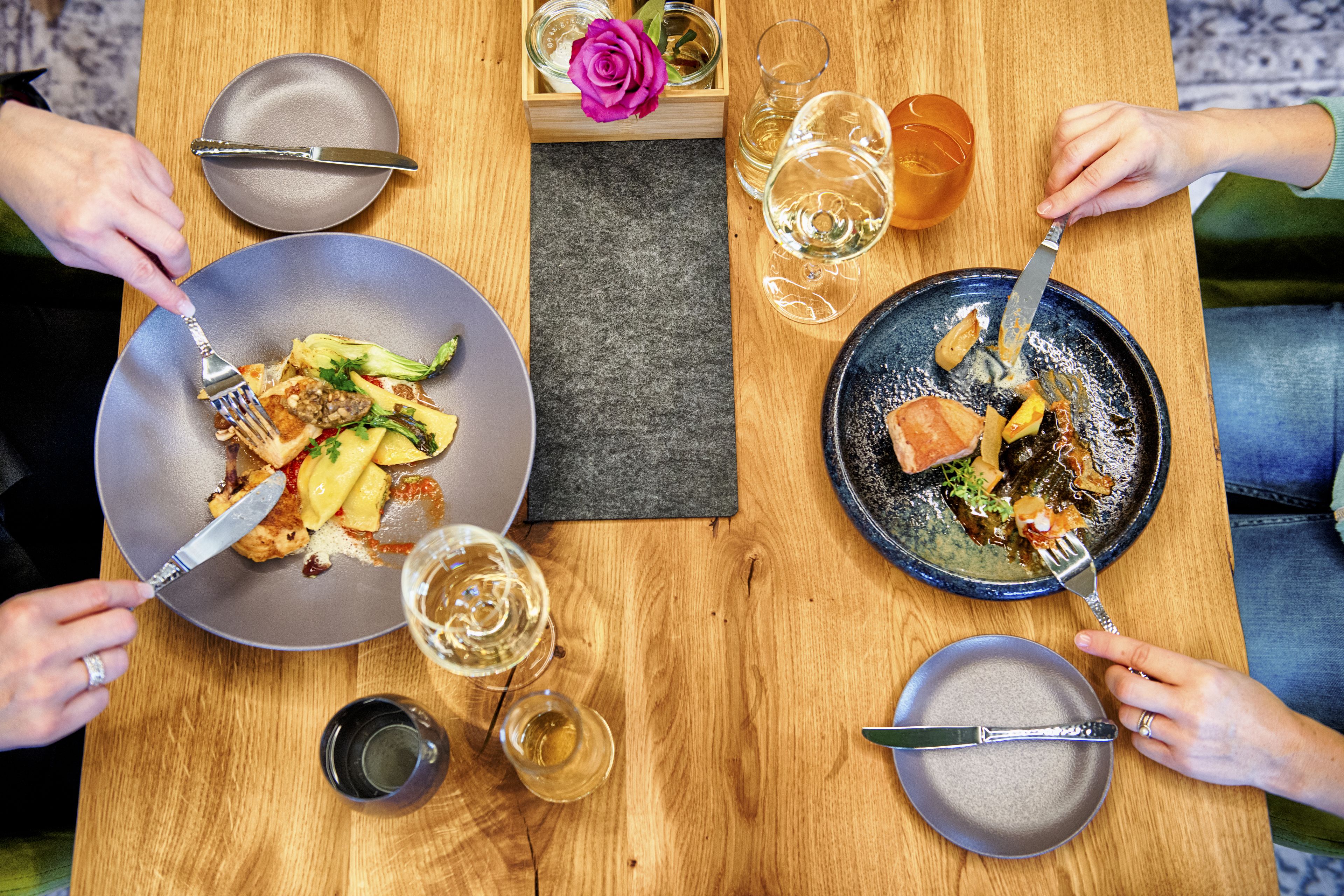 A wooden dining table with plates of food, glasses of wine, and cutlery.