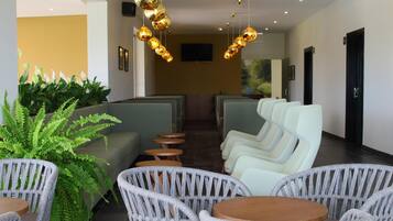A modern hotel lobby with wicker chairs, a sofa, and a TV on the wall.