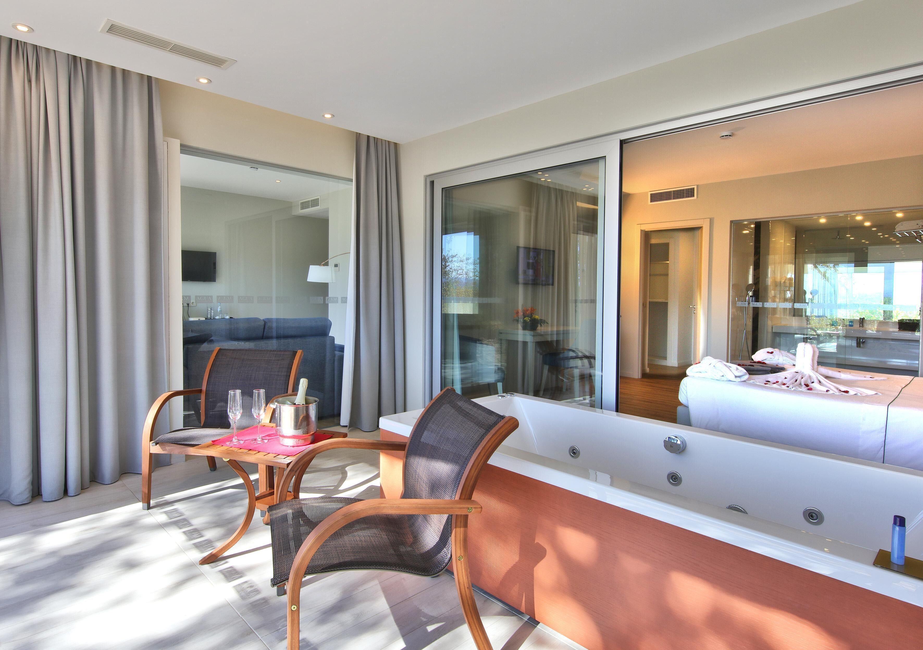 Ein modernes Hotelzimmer mit einem großen Fenster, einem Sofa, einem Tisch mit einer Flasche und einer Badewanne.