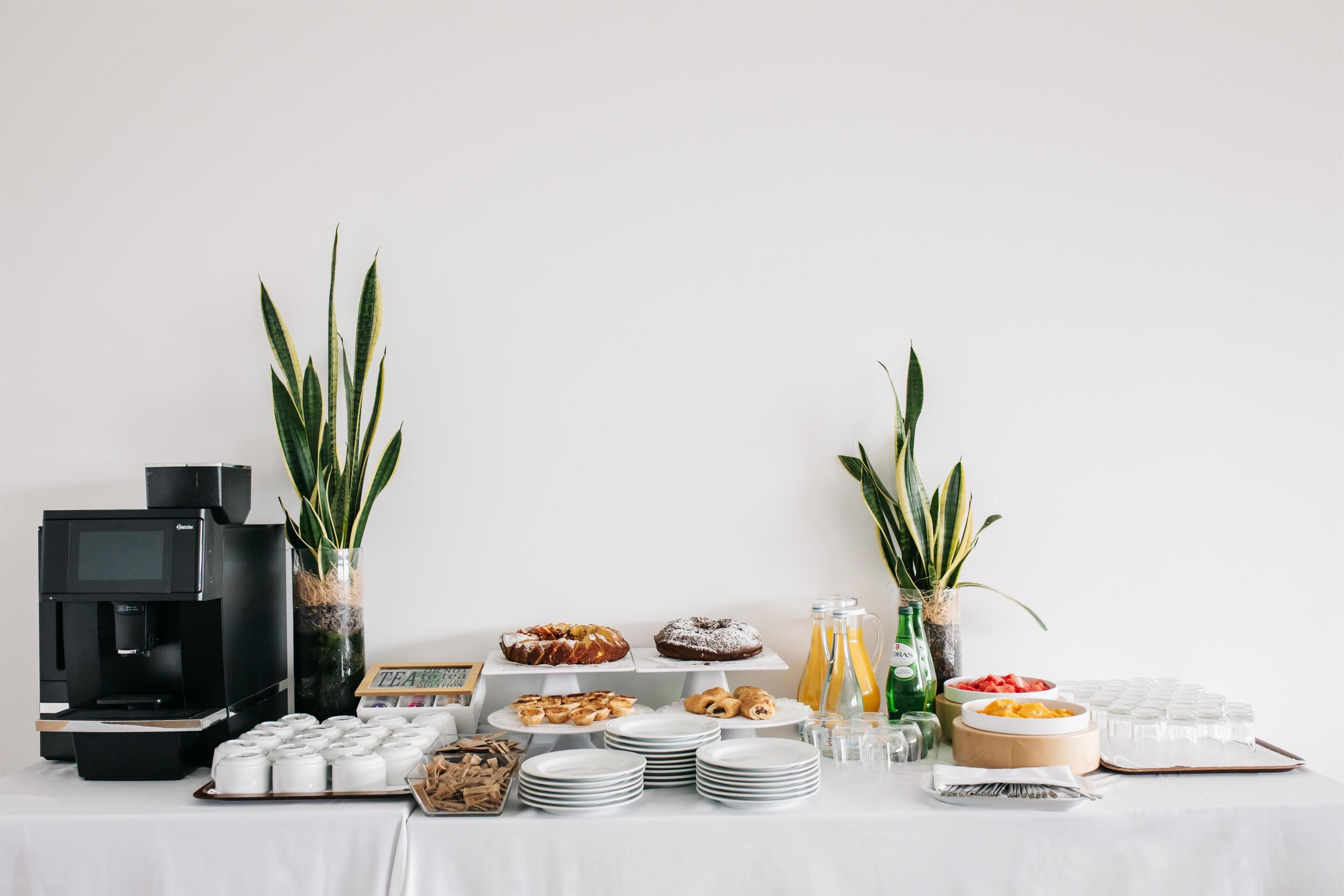 A buffet table with various food items, a coffee machine, and decorative plants.