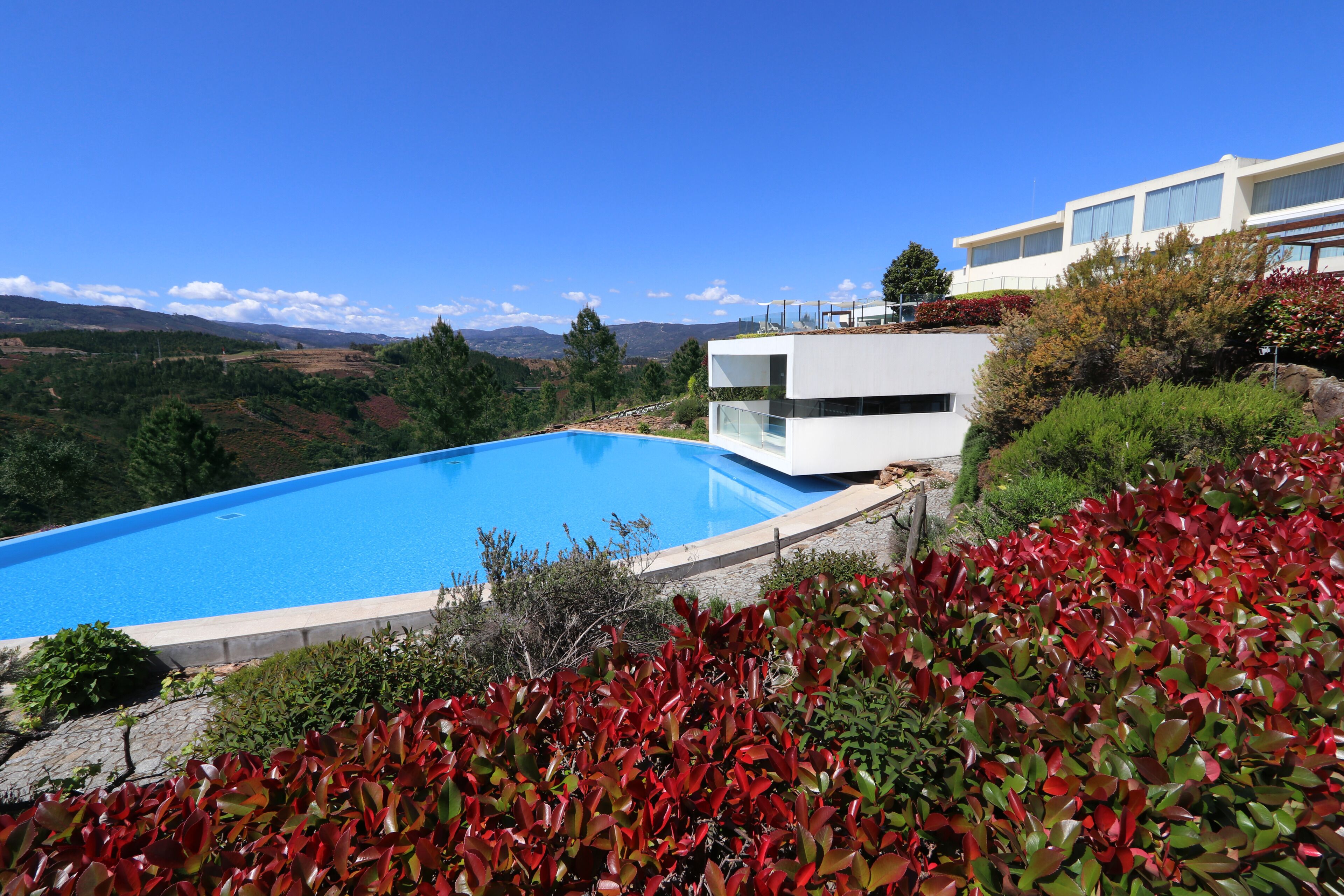 A modern pool area with a clear blue pool, surrounded by lush greenery and a view of distant mountains.