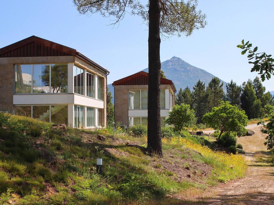 Zwei moderne Gebäude mit großen Fenstern, eingebettet in eine natürliche Landschaft, im Hintergrund ein Berg.