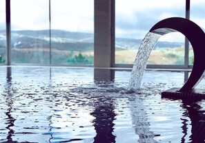 Una fuente de agua interior moderna con un caño curvo, reflejado sobre una superficie húmeda.