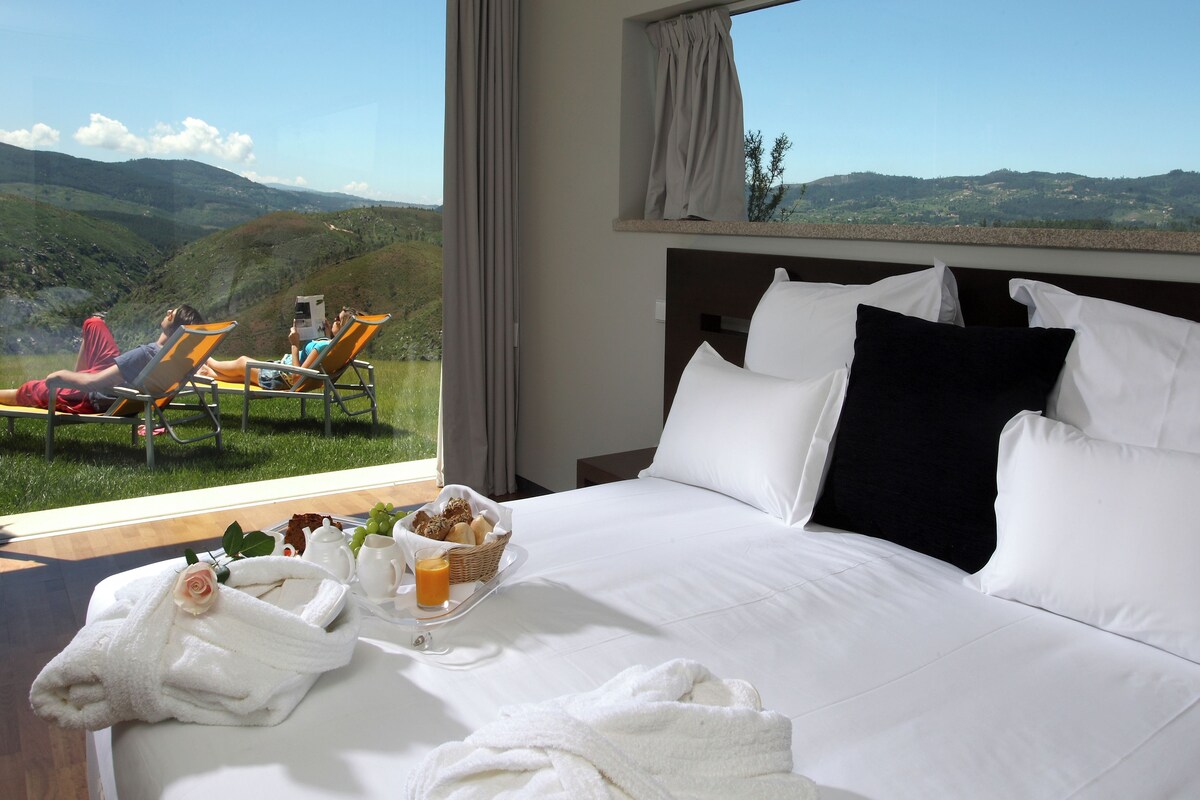 Ein Hotelzimmer mit einem großen Bett, einem Frühstücksbrett und Blick auf eine Berglandschaft.