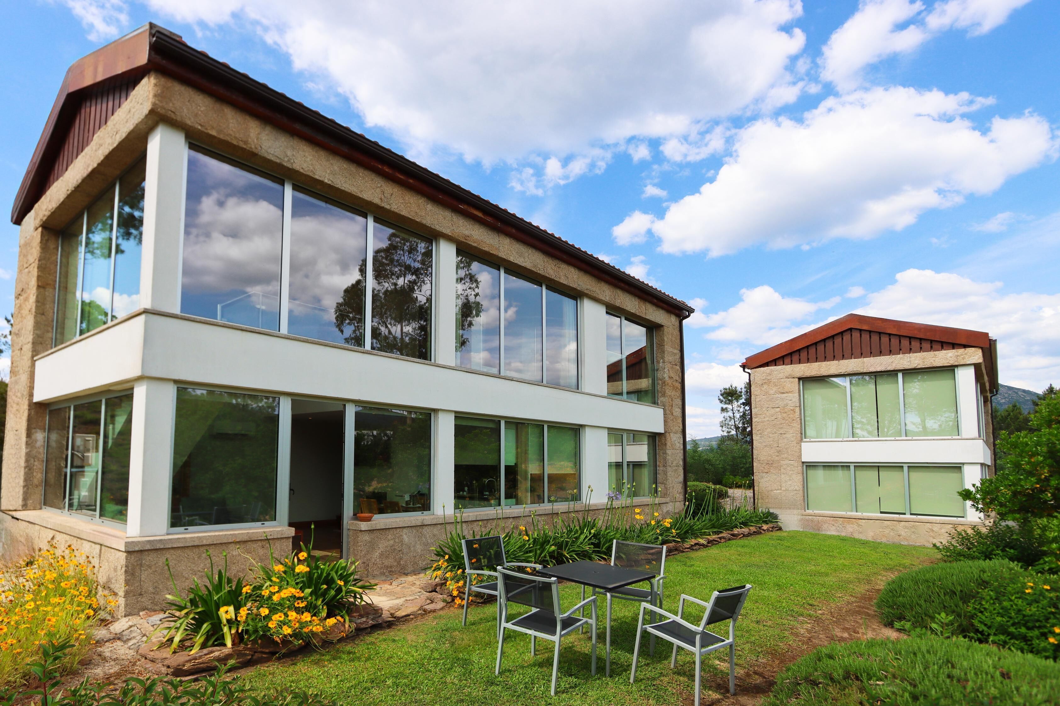 Una casa moderna de dos pisos con amplios ventanales y un patio con mobiliario exterior.