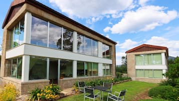 Una casa moderna de dos pisos con amplios ventanales y un patio con mobiliario exterior.