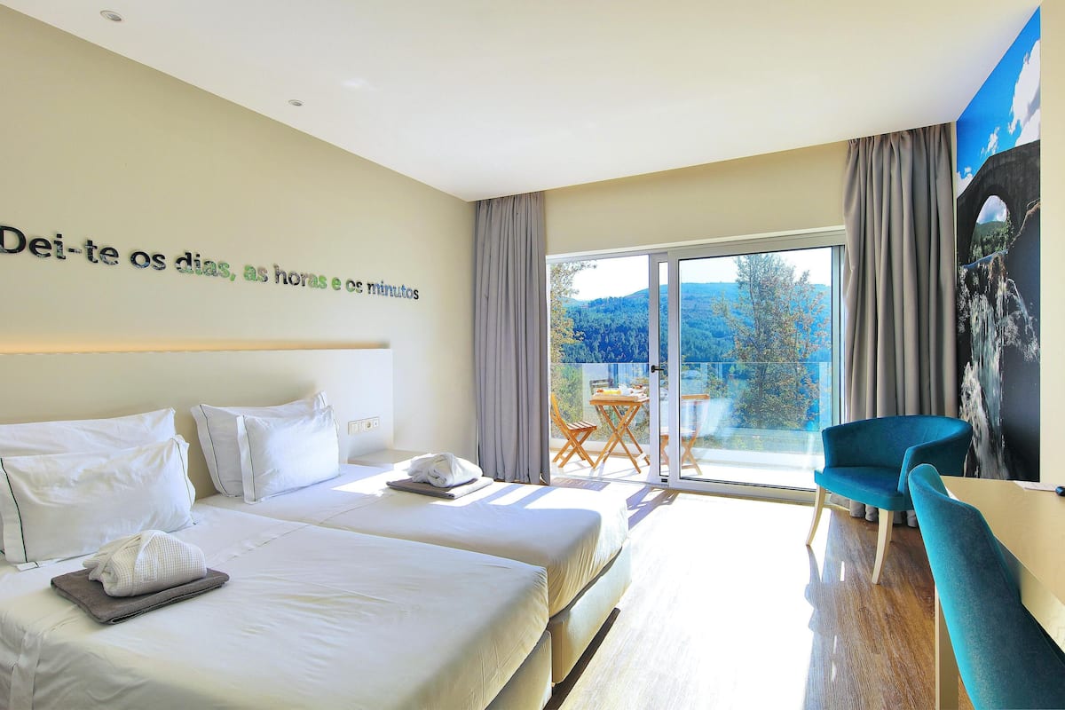 Ett hotellrum med två sängar, ett skrivbord, en stol och ett stort fönster med utsikt över omgivningarna.