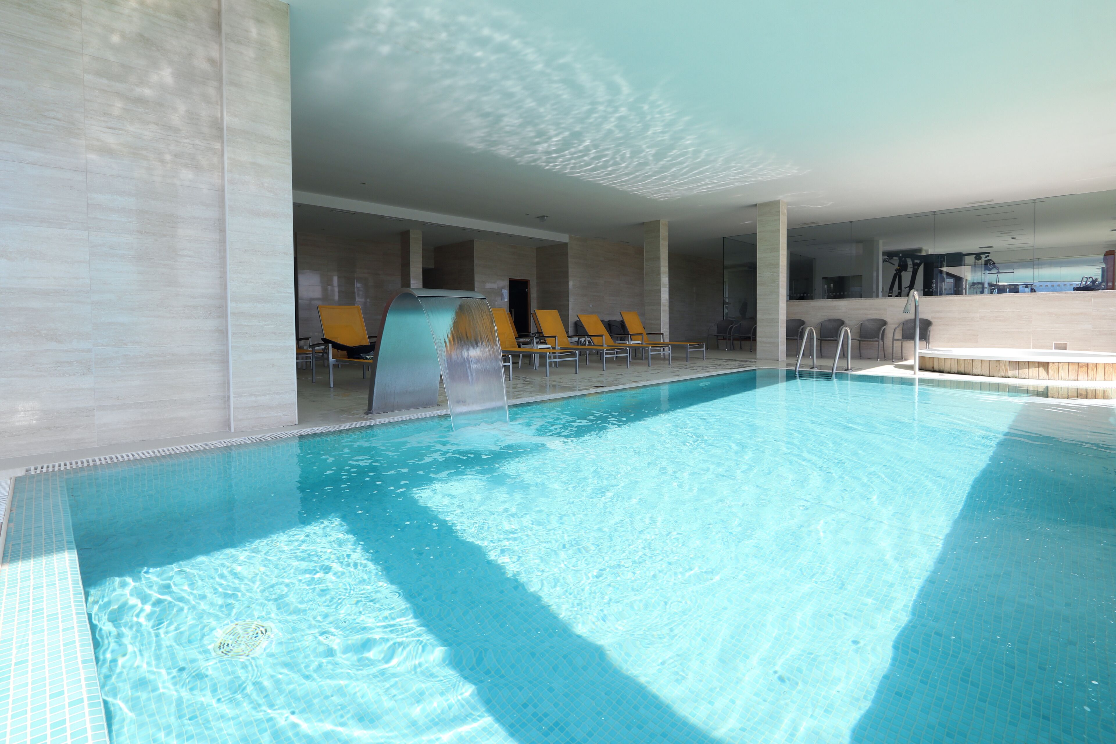 Una piscina con agua cristalina, rodeada de sillas de descanso y un diseño interior moderno.