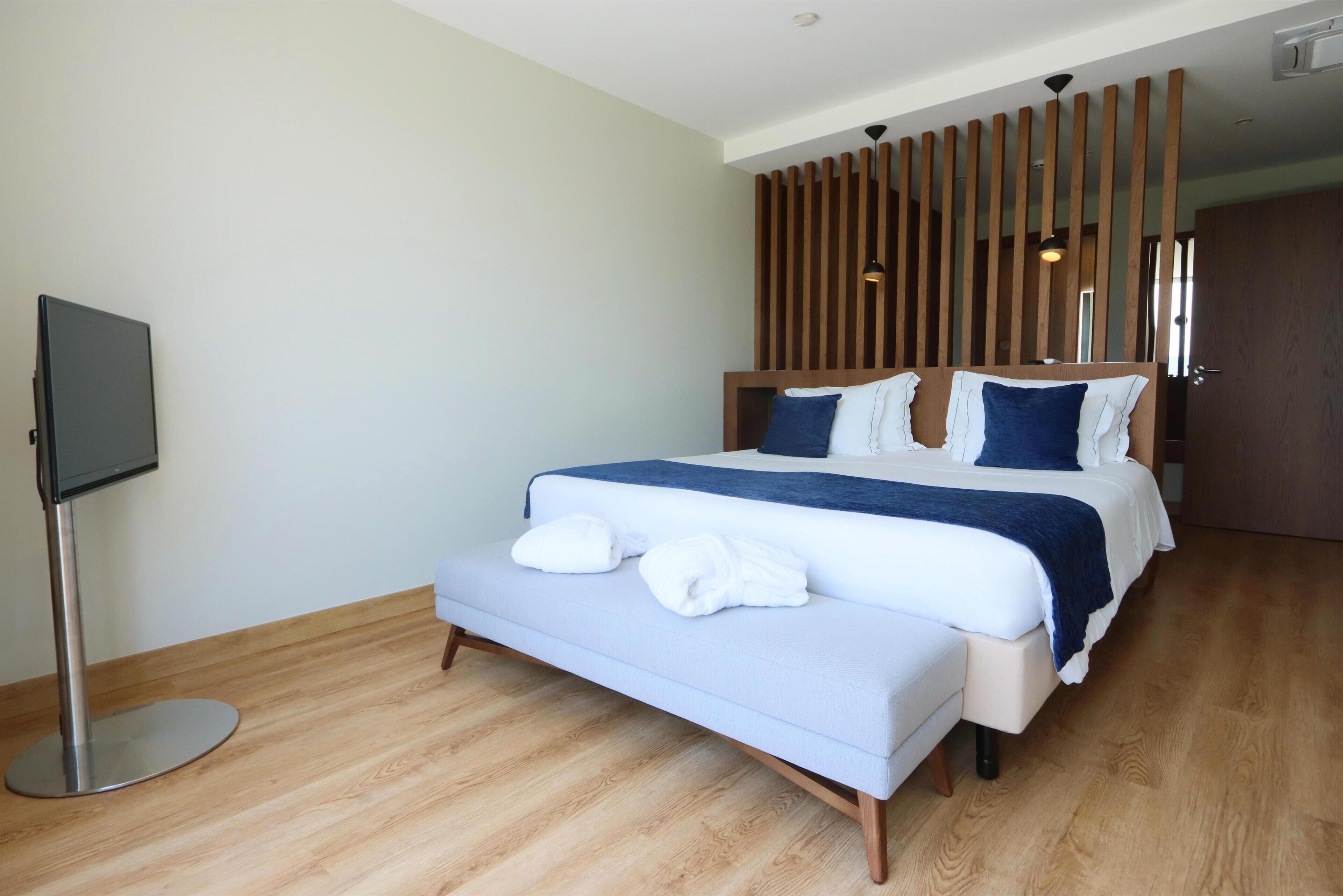 A modern hotel room with a large bed, a flat-screen TV, and a wooden partition wall.