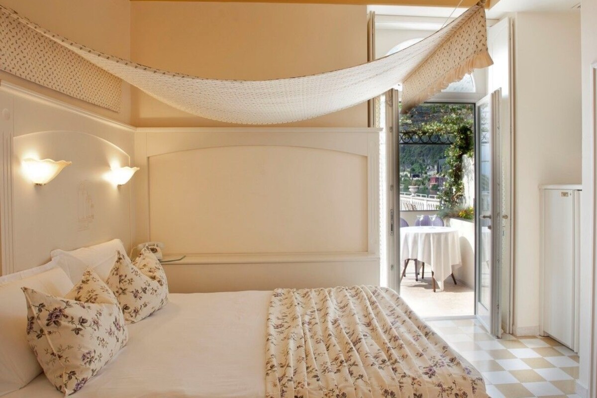 Een slaapkamer met een bed, bloemenkussens, een hemelbed en uitzicht op een terras.