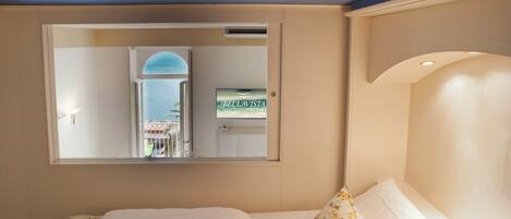 A hotel room with a large bed, a mirror reflecting the room, and a sign for 'BELTAVISTA' on the wall.