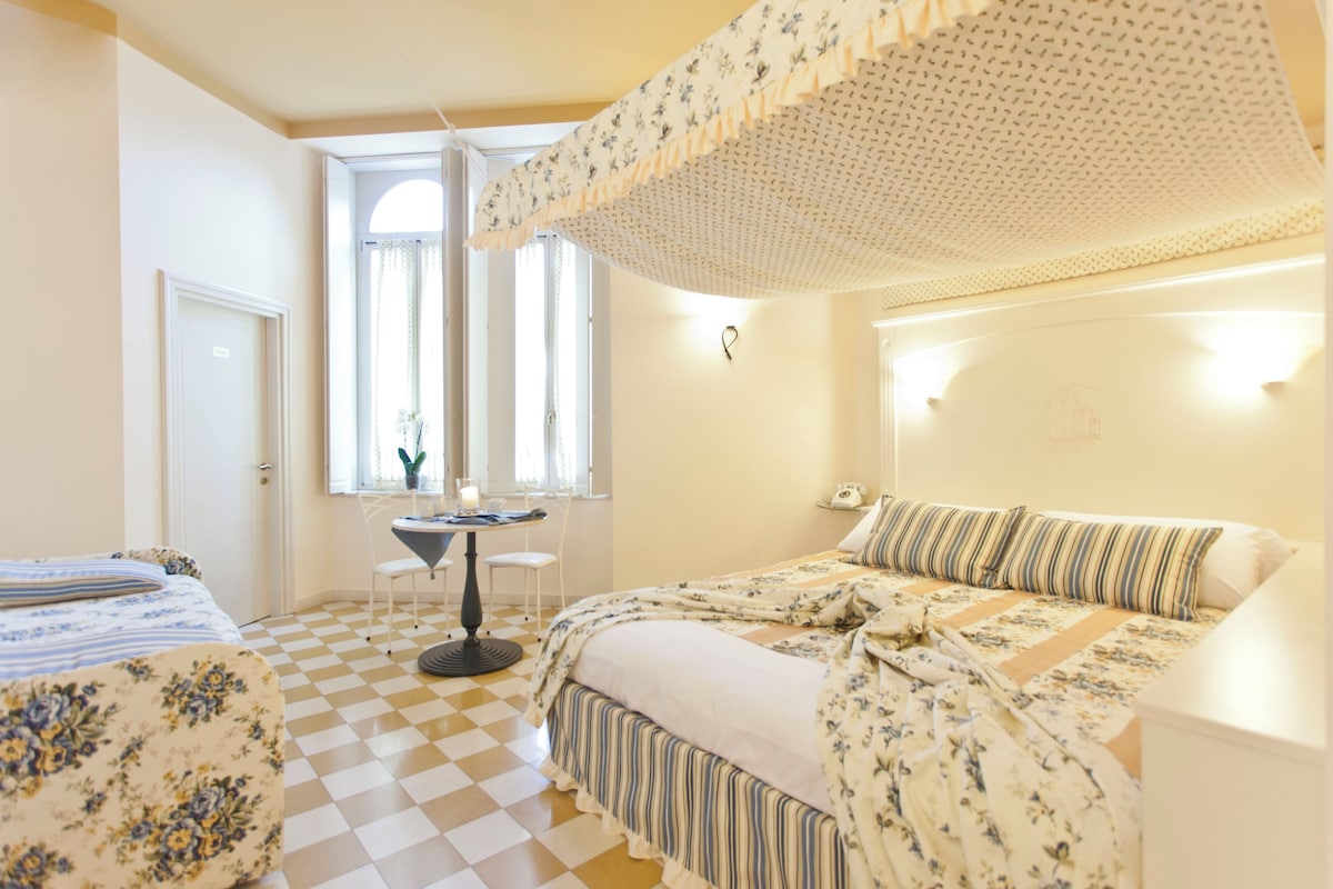 Un dormitorio con piso a cuadros, una cama con ropa de cama floral, un escritorio con silla y una ventana con cortinas.