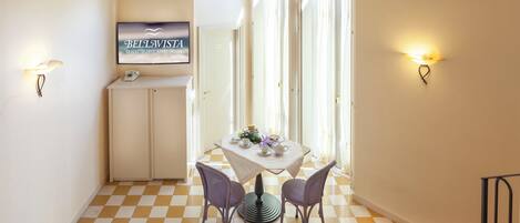 A hotel room with a checkered floor, a dining table with two chairs, a television, and a cabinet.