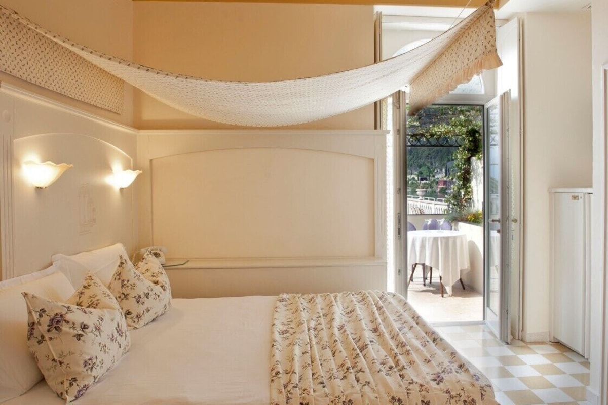Un dormitorio con cama, almohadas florales, dosel y vistas a un patio exterior.