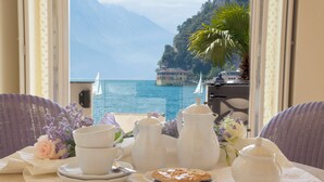 A table set with white tea serviceware and a plate of cookies, overlooking a lake with boats and a building on a hillside. - Bellavista Lakefront (Riva del Garda)