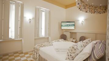 A hotel room with a checkered floor, a bed with floral bedding, a television on the wall, and a window with curtains.