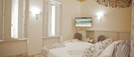 A hotel room with a checkered floor, a bed with floral bedding, a television on the wall, and a window with curtains.
