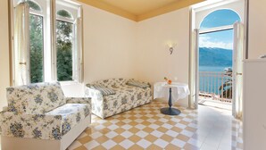 A room with a checkered floor, a sofa, a small table, and a view of the sea through an open door. - Bellavista Lakefront (Riva del Garda)