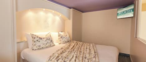 A neatly made bed with floral bedding, a headboard with built-in lighting, and a sign for 'BELLA VISTA' on the wall.