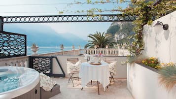 Une terrasse avec un jacuzzi, une table et des chaises, et une vue sur la mer.