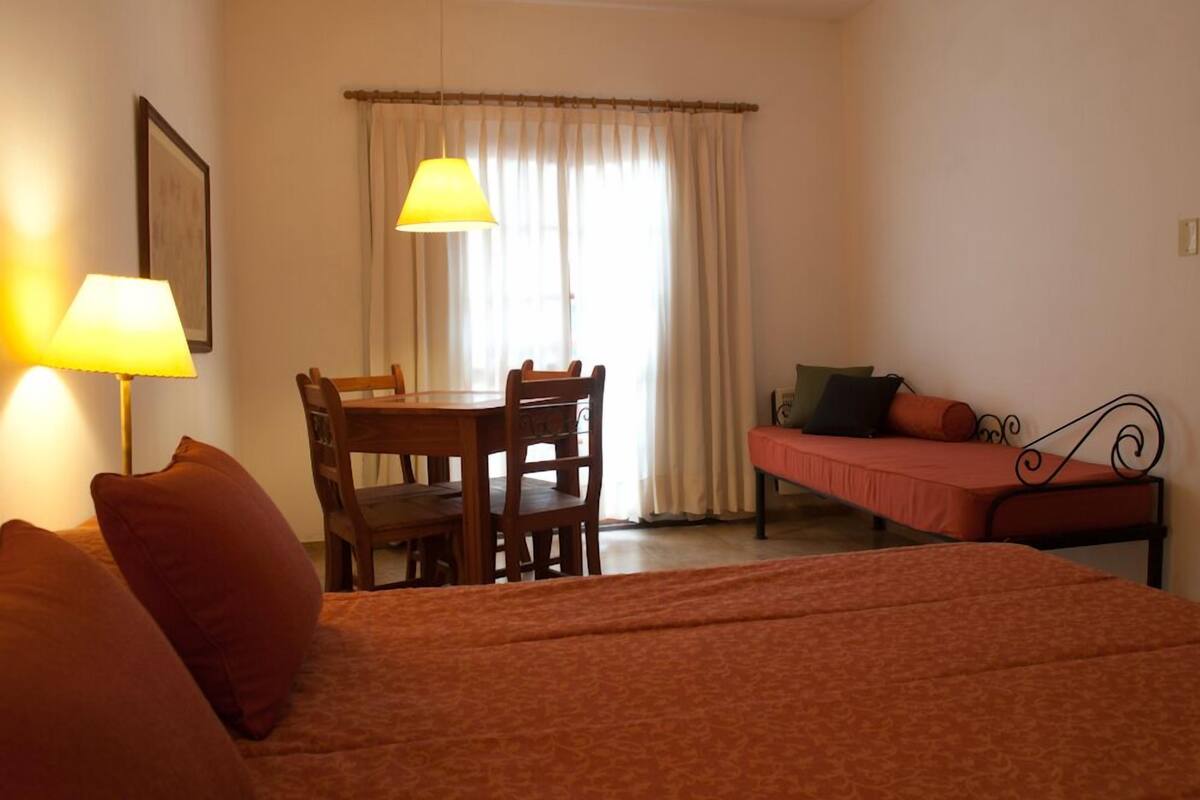 A room with a bed, a table with chairs, a sofa, and a window with curtains.