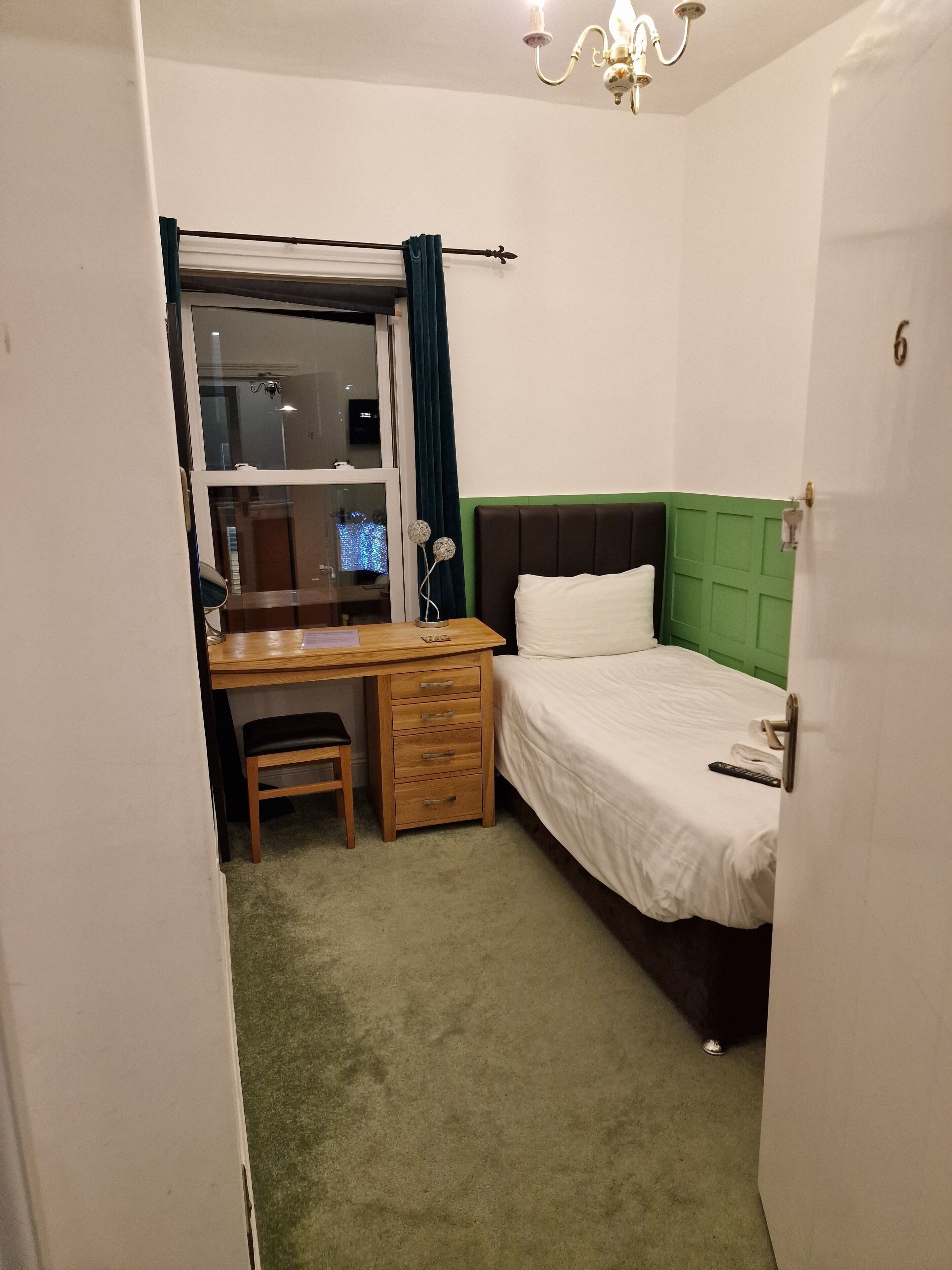 A compact hotel room with a single bed, a desk with a chair, a small table, and a window with curtains.
