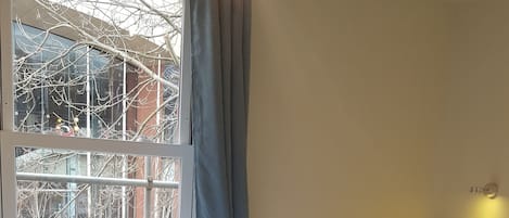 Habitación de hotel con cama, ventana con cortinas, cabecero y lámpara fijada a la pared.