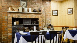 Un comedor con paredes de ladrillo, chimenea y paneles de madera. Hay mesas dispuestas con manteles blancos y sillas.
