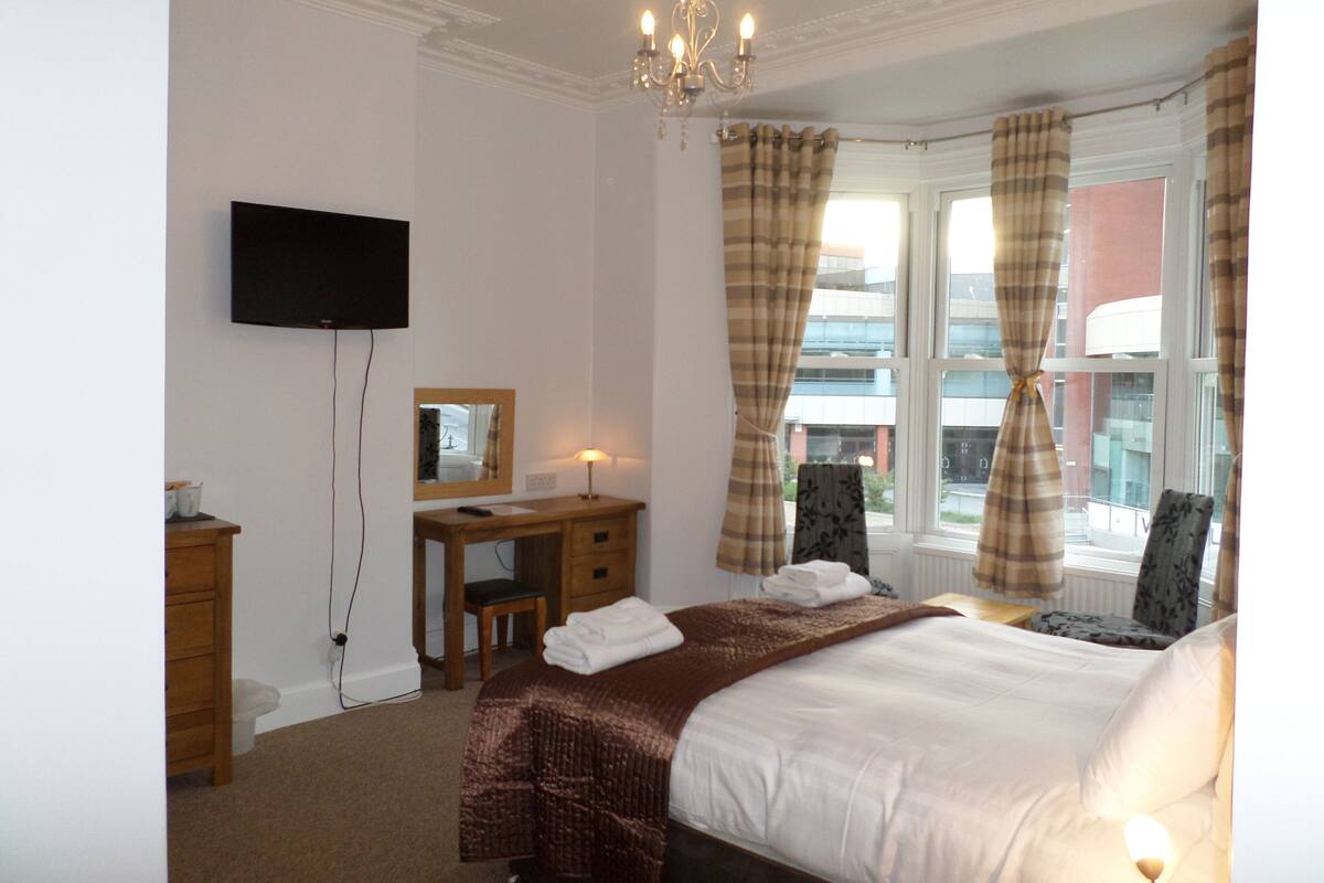 A hotel room with a bed, a desk, a chair, a television, and a window with curtains.